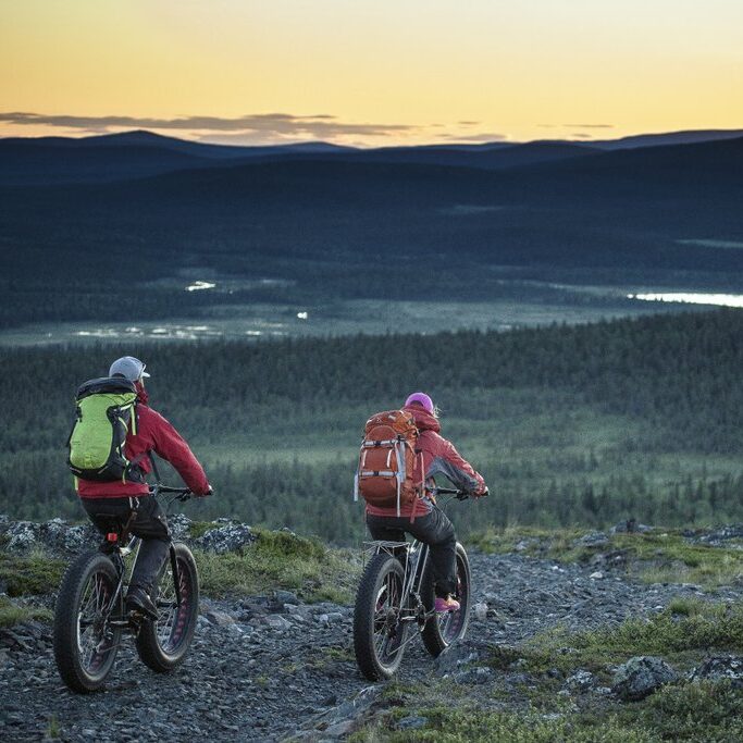 Two persons with bikes journeying in fell landscape in Muonio, Finnish Lapland