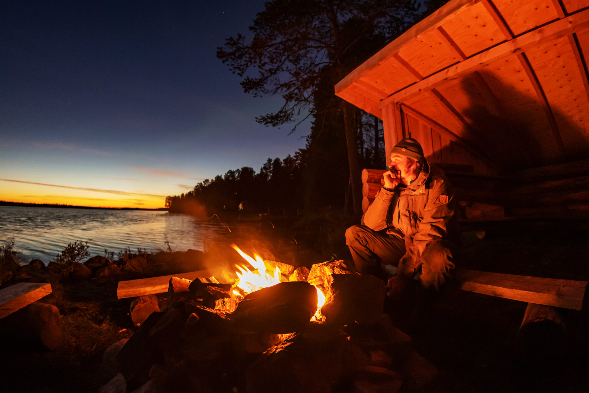 Guest enjoying an evening campfire by a lake at Harriniva Hotels & Safaris in Muonio, Lapland, Finland