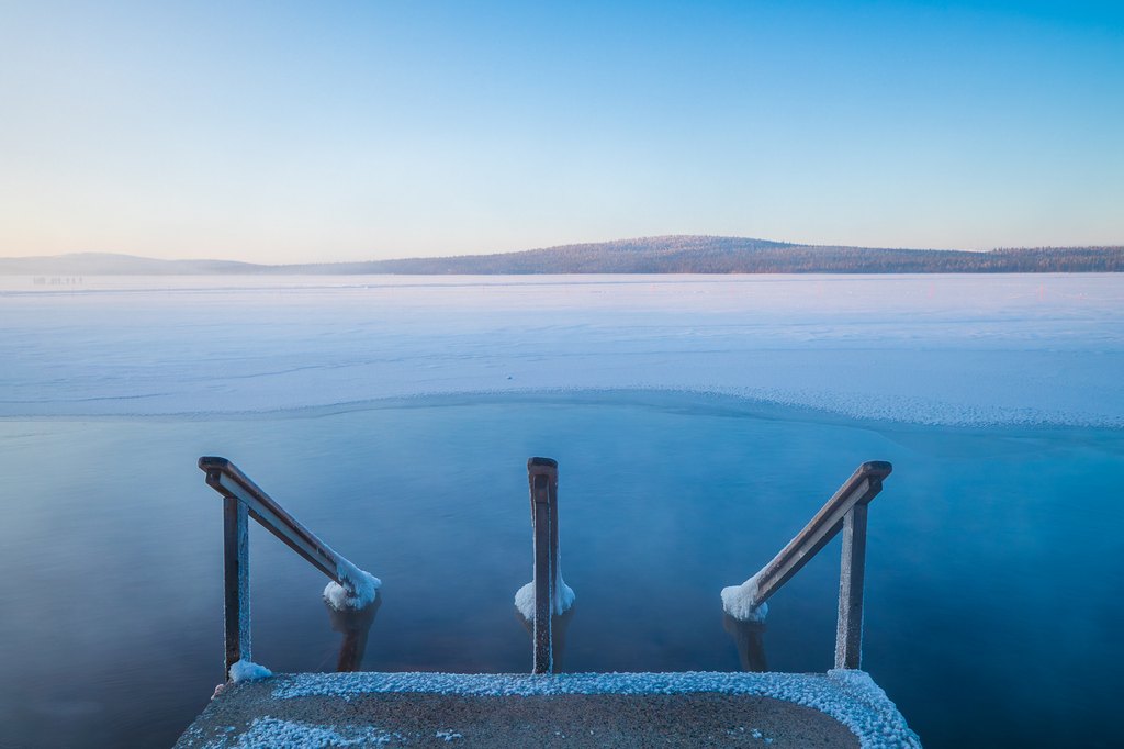 Steps leading into wintery ice hole with winter surroundings at Arctic Sauna World, Lapland, Finland