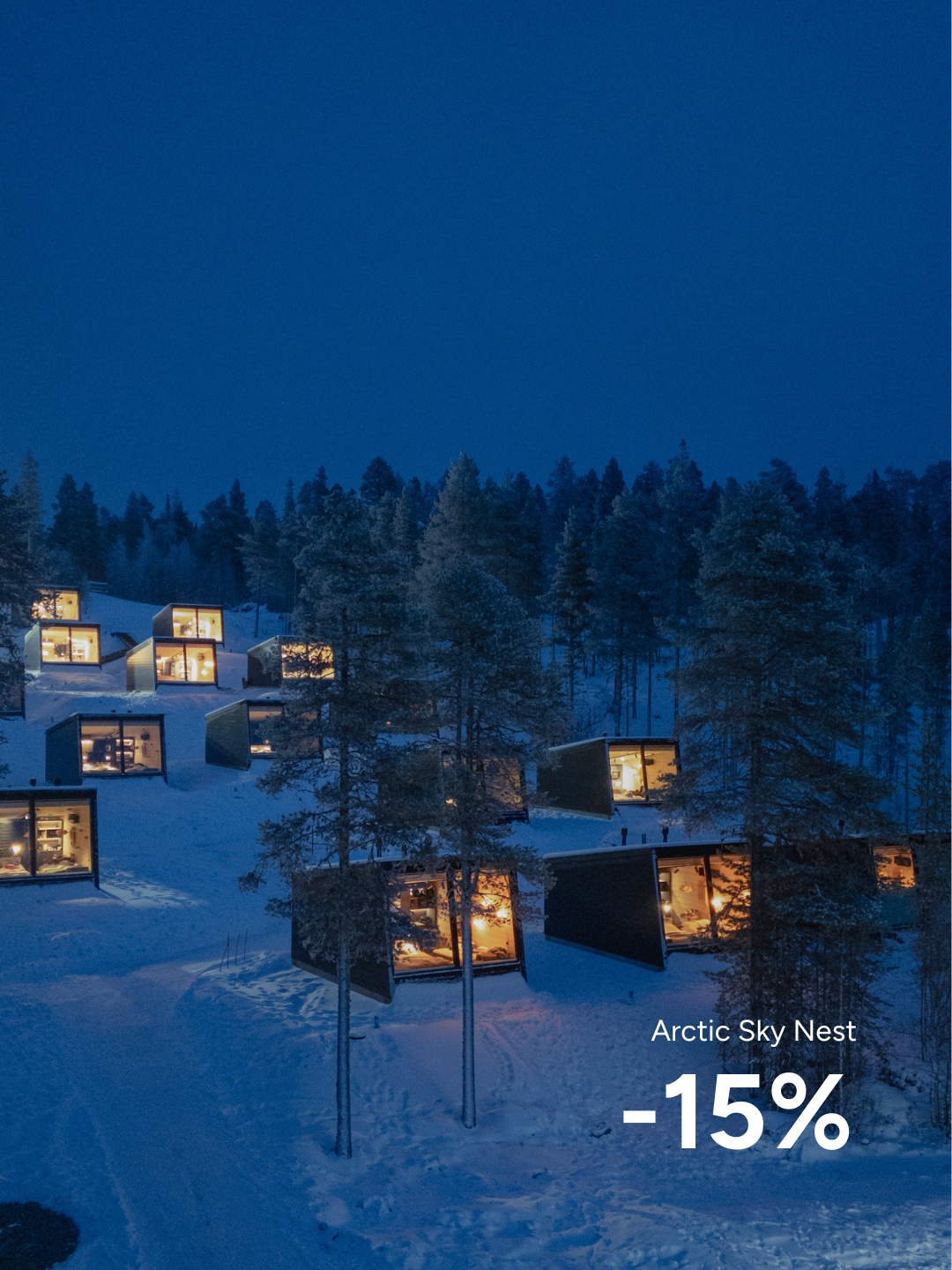 FI: Lumisessa Lapin metsämaisemassa Jeris Lakeside Resortin Arctic Sky Nest -majoitukset hehkuvat lämpimästi sinisen hetken hämärässä; kuvateksti ilmoittaa talvitarjouksen “Arctic Sky Nest -15%”. EN: In a snowy Lapland forest landscape, Jeris Lakeside Resort’s Arctic Sky Nest cabins glow warmly in the blue-hour dusk; overlay text highlights the winter offer “Arctic Sky Nest -15%”.