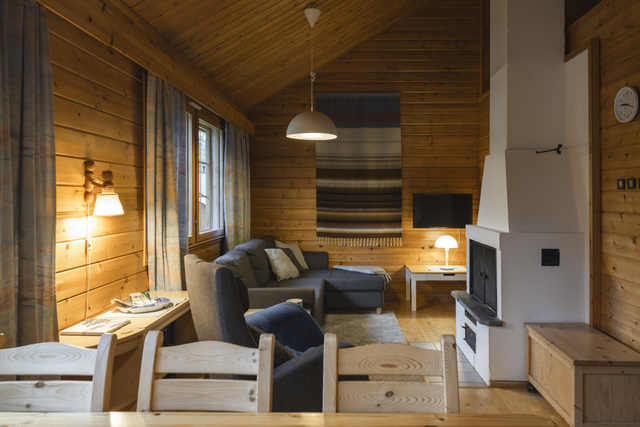 Jeris Lakeside Resortin lomamökin oleskelutila Lake Jerisjärven läheisyydessä Lapissa. Luonnonpuusta rakennettu hirsimökki tarjoaa viihtyisän sohvaryhmän, takan, ruokailualueen ja lämpimän valaistuksen. Suuret ikkunat tuovat sisään luonnonvaloa ja metsän rauhan, luoden kodikkaan ja rauhallisen mökkimajoituskokemuksen Lapin luonnon keskellä.

In English (EN):
The living area of the Forest cabin accommodation at Jeris Lakeside Resort near Lake Jerisjärvi in Finnish Lapland. The log-built wooden cabin features a cozy seating area, fireplace, dining space, and warm lighting. Large windows invite natural light and forest views inside, creating a peaceful and comfortable cabin stay surrounded by Lapland’s nature.