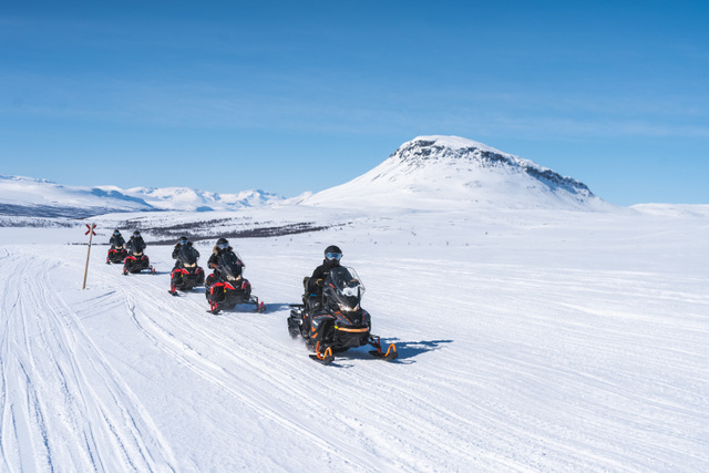 FI: Moottorikelkkaretki etenee jonossa halki avaran tunturiylängön kohti lumihuippuista tunturia Lapissa – Snowmobile Expedition osana Harriniva Hotels & Safarisin Summit Adventure Arctic All-Inclusive -täyshoitolomapakettia Muoniossa.
EN: A snowmobile expedition rides in a line across a vast fell plateau toward a snow-capped peak in Lapland—Snowmobile Expedition as part of Harriniva Hotels & Safaris’ Summit Adventure Arctic All-Inclusive holiday package in Muonio.