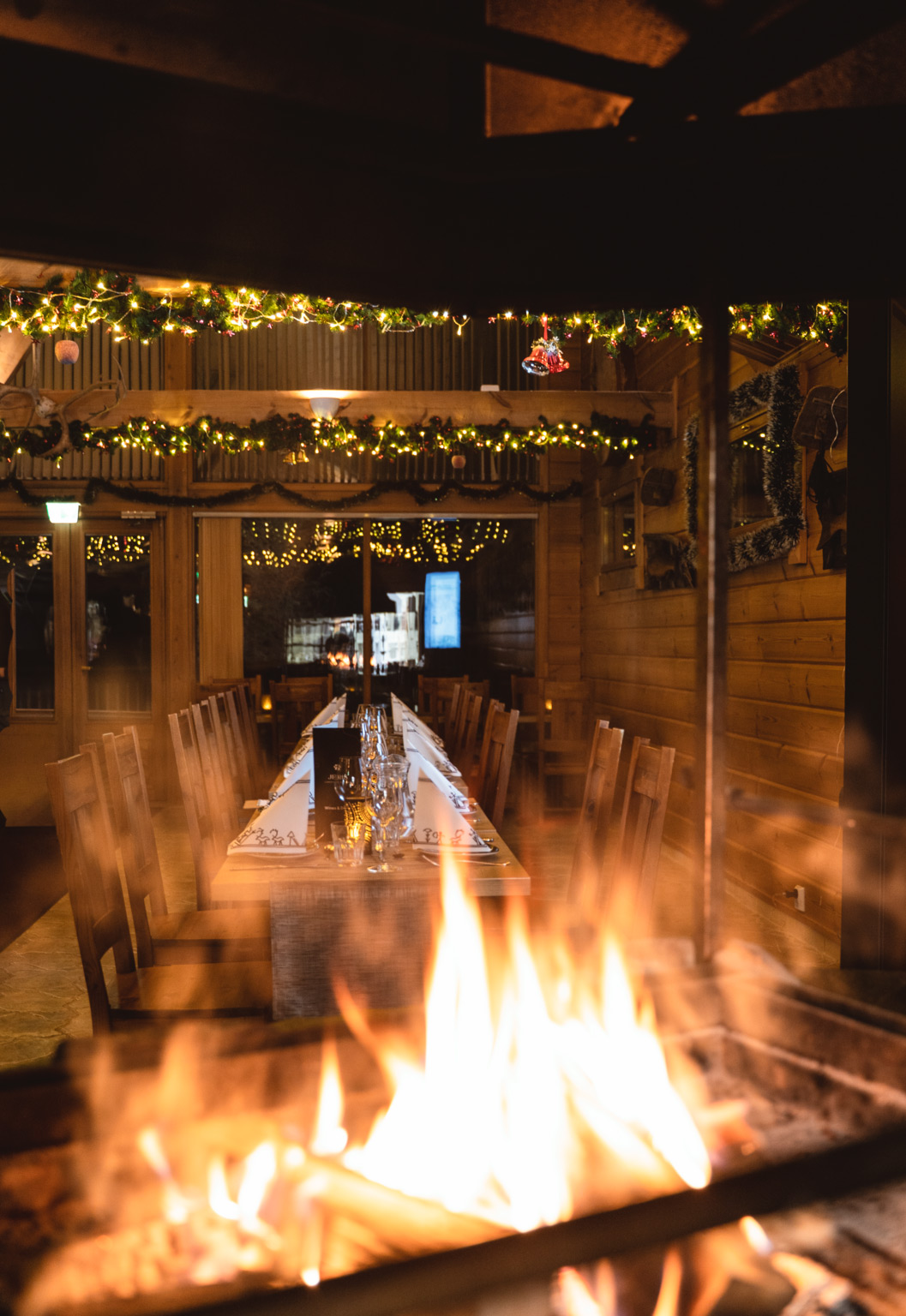 Jeris Lakeside Resortin Harriniva Signature Dinner Experience Arctic Sauna Worldissa Lake Jerisjärven läheisyydessä Muoniossa Lapissa. Tunnelmallinen ravintolasali on koristeltu kynttilöin ja valoin, pitkä pöytä on katettu huolella ja avotulen liekit luovat lämpimän ja intiimin ilmapiirin. Illallinen edustaa Harriniva Hotels & Safarisin korkeatasoista lappilaista ruokakulttuuria luonnon keskellä. In English (EN): The Harriniva Signature Dinner Experience at Jeris Lakeside Resort’s Arctic Sauna World near Lake Jerisjärvi in Muonio, Finnish Lapland. The atmospheric dining space features candlelight, festive decorations, a beautifully set long table, and open fire flames creating a warm and intimate ambiance. This dining experience reflects the high-quality Lapland cuisine of Harriniva Hotels & Safaris in a unique natural setting.