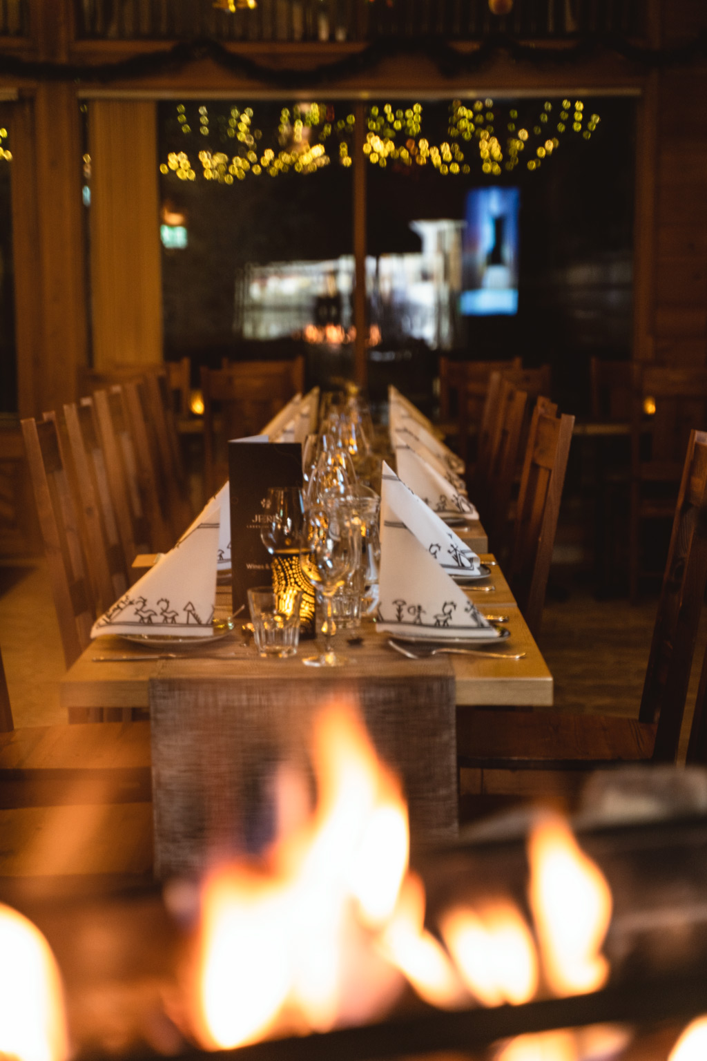 Jeris Lakeside Resortin Harriniva Signature Dinner Experience Arctic Sauna Worldissa Lake Jerisjärven läheisyydessä Muoniossa Lapissa. Tunnelmallinen ravintolasali on koristeltu kynttilöin ja valoin, pitkä pöytä on katettu huolella ja avotulen liekit luovat lämpimän ja intiimin ilmapiirin. Illallinen edustaa Harriniva Hotels & Safarisin korkeatasoista lappilaista ruokakulttuuria luonnon keskellä.
In English (EN):
The Harriniva Signature Dinner Experience at Jeris Lakeside Resort’s Arctic Sauna World near Lake Jerisjärvi in Muonio, Finnish Lapland. The atmospheric dining space features candlelight, festive decorations, a beautifully set long table, and open fire flames creating a warm and intimate ambiance. This dining experience reflects the high-quality Lapland cuisine of Harriniva Hotels & Safaris in a unique natural setting.