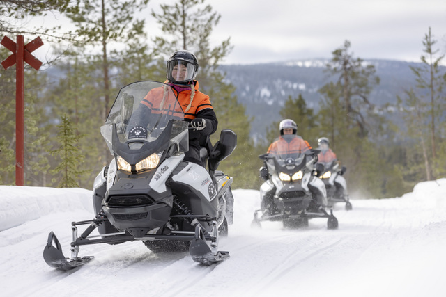 FI: Moottorikelkkasafari etenee talvisella metsäuralla Muoniossa, Lapissa; etualalla ajaja ja taustalla kaksi kelkkaa lumipöllyn keskellä – Snowmobile Experience osana Bucket List Christmas Breakia, all-inclusive holiday package Harriniva Hotels & Safarisilla.
EN: A snowmobile safari rides along a winter forest trail in Muonio, Lapland, with one rider in front and two snowmobiles following in snowy spray—Snowmobile Experience as part of the Bucket List Christmas Break, an all-inclusive holiday package with Harriniva Hotels & Safaris.