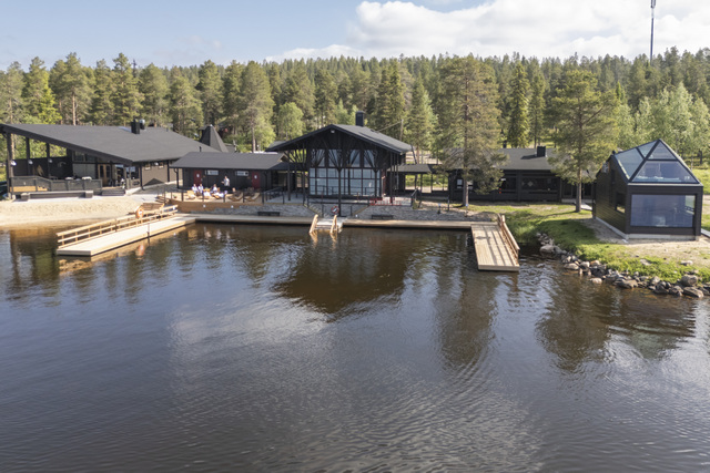 FI: Jeris Lakeside Resortin Arctic Sauna World näkyy järven rannalla Muoniossa Lapin kesässä, puisine laitureineen, modernine rakennuksineen ja rauhallisine metsämaisemineen. Harriniva Hotels & Safaris tarjoaa kesää Lapissa luonnon, järvimaisemien ja rentouttavien saunaelämysten äärellä. EN: Arctic Sauna World at Jeris Lakeside Resort is set on the lakeshore in Muonio during summer in Lapland, with wooden docks, modern buildings, and peaceful forest surroundings. Harriniva Hotels & Safaris offers summer in Lapland with nature, lake views, and relaxing sauna experiences.