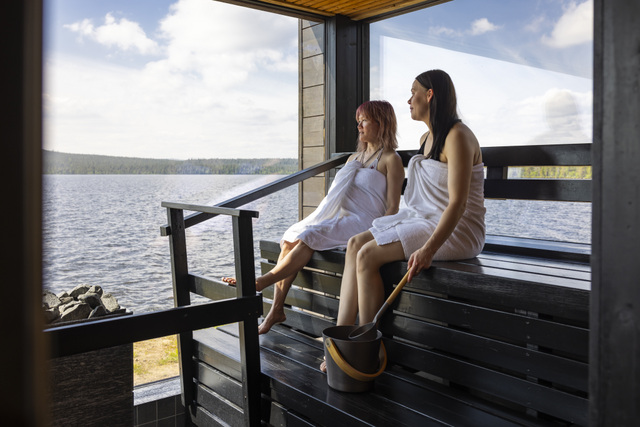 FI: Kaksi saunavierasta istuu lauteilla järven rannalla ja ihailee kesäistä maisemaa Lapissa. Harriniva Hotels & Safarisin Arctic Sauna World tarjoaa rentouttavan kesäelämyksen Lapissa järvinäköalojen, saunan ja luonnon rauhan keskellä.
EN: Two sauna guests sit on the benches by the lake and enjoy the summer view in Lapland. Arctic Sauna World by Harriniva Hotels & Safaris offers a relaxing summer in Lapland with lakeside sauna views, peaceful nature, and a calming atmosphere.