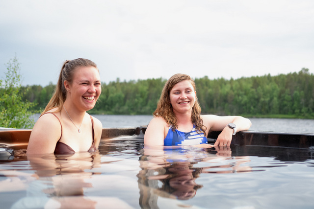 Suomi: Kaksi vierasta rentoutuu ulkoporealtaassa joen rannalla Muoniossa, Lapissa, vehreän kesämaiseman keskellä. Rauhallinen sauna- ja jacuzzihetki luonnon äärellä tuo esiin pohjoisen kesän hyvinvoinnin ja elämyksellisen majoituksen. Harriniva Hotels & Safaris ja Harriniva Adventure Resort tarjoavat kesäelämyksiä Muoniossa, Lapissa, yhdistäen riverside saunan, jacuzzin, luonnonrauhan ja arktisen tunnelman.
English: Two guests relax in an outdoor jacuzzi by the river in Muonio, Lapland, surrounded by lush summer scenery. This peaceful sauna and hot tub moment in nature highlights northern summer wellness and experience-based accommodation. Harriniva Hotels & Safaris and Harriniva Adventure Resort offer summer experiences in Muonio, Lapland, combining a riverside sauna, jacuzzi, peaceful nature, and authentic Arctic atmosphere.